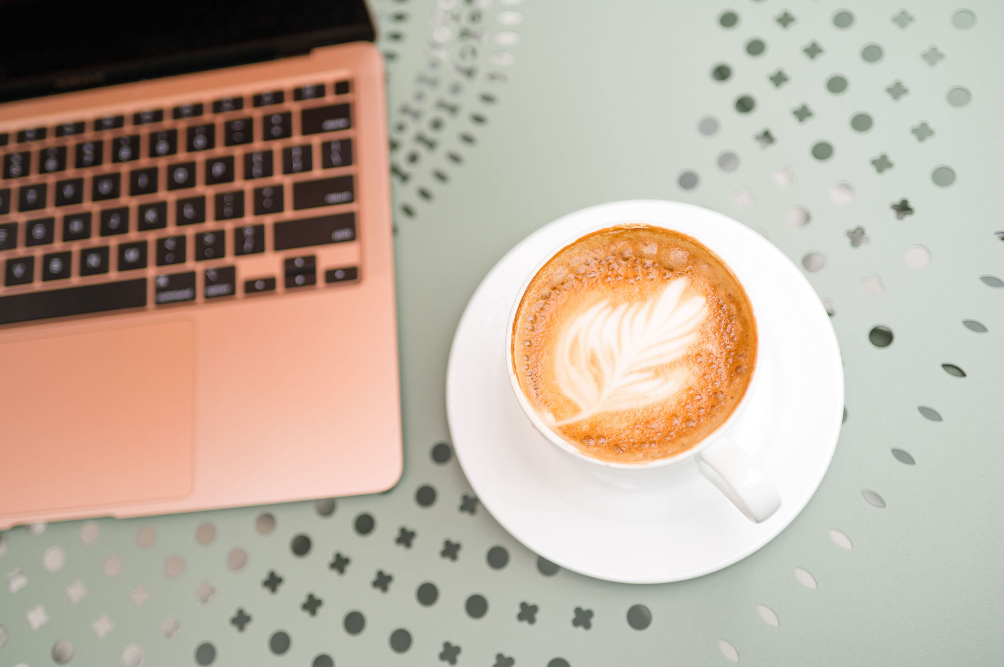 Laptop and latte on a sage table — tools for sharpening your marketing strategy.